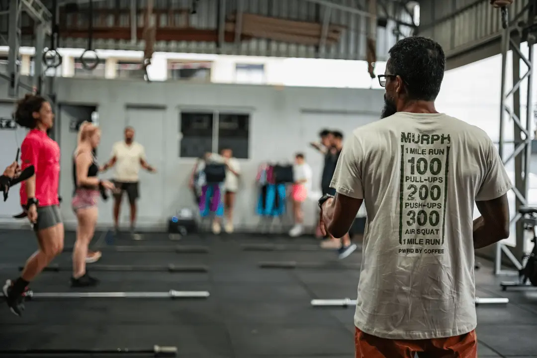 Coach do CrossFit Canasvieiras orienta aquecimento com corda no box em Florianópolis; alunos ao fundo e barras no chão.