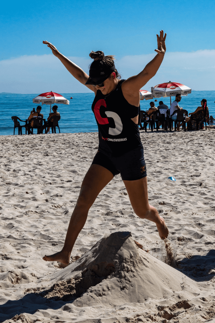 Aluna do CrossFit Canasvieiras executa salto pliométrico na areia da praia em Florianópolis durante treino ao ar livre.