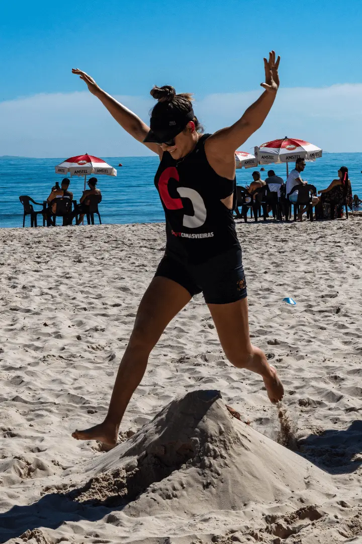 Aluna do CrossFit Canasvieiras executa salto pliométrico na areia da praia em Florianópolis durante treino ao ar livre.